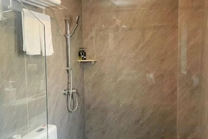 A shower with a glass enclosure, a towel hanging on the wall, and a small shelf with toiletries. - Home Inn Plus (Wuhan Chuhe Hanjie Metro Station Branch) (Wuhan)