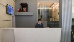A reception desk with a man standing behind it, a digital screen, and a decorative shelf above. - Home Inn Plus (Wuhan Chuhe Hanjie Metro Station Branch) (Wuhan)