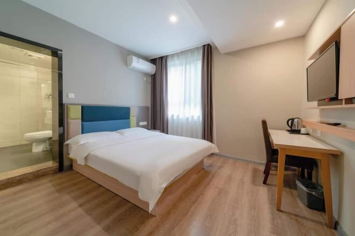 Ein Hotelzimmer mit einem Bett, einem Schreibtisch, einem Stuhl, einem Fernseher und einer Duschkabine.