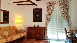 A cozy living room with a sofa, a wooden cabinet, a lamp, and a window with curtains. - Posada Alpujarra Sol (Orgiva)