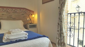 A neatly made bed with folded towels, a bedside lamp, and a view of a balcony with a wrought iron railing. - Posada Alpujarra Sol (Orgiva)