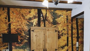 A room with a wooden wardrobe, a desk with a lamp, and a wall mural of autumn trees. - Posada Alpujarra Sol (Orgiva)