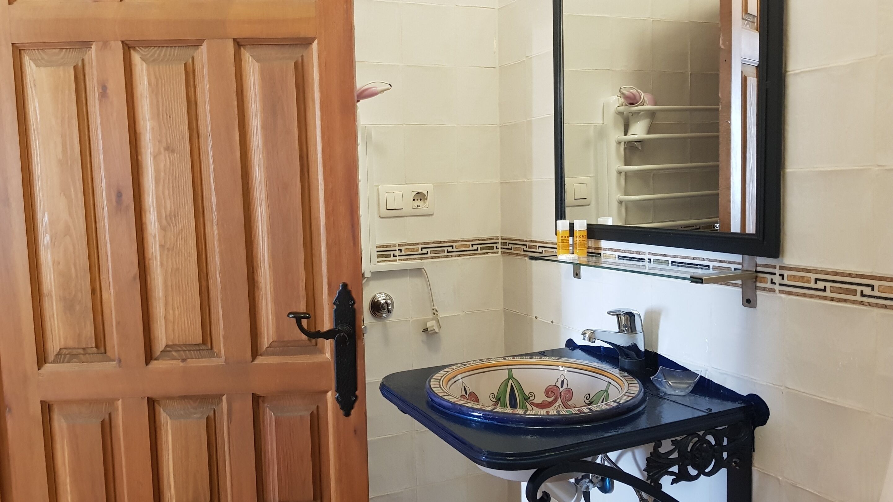 A bathroom with a wooden door, a sink with a decorative basin, a mirror, and a towel rack.