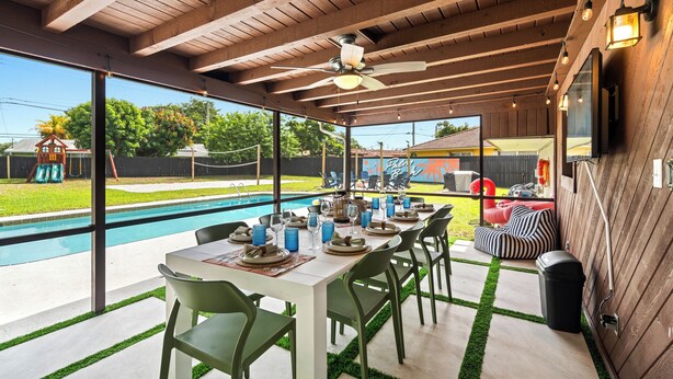 Un espace extérieur abrité, aménagé pour les repas, avec vue sur la piscine, des poutres en bois au plafond et des chaises vertes.