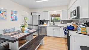 Une cuisine moderne avec des armoires blanches, des appareils en acier inoxydable et un banc en bois.