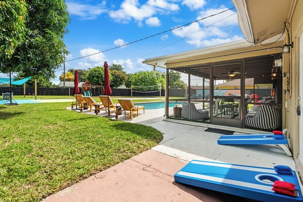 A backyard with a pool, lounge chairs, and a covered patio area.