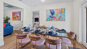 Un espace repas moderne avec une table en verre, des chaises roses et des œuvres d’art abstraites accrochées aux murs.
