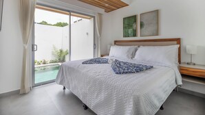 Ein Schlafzimmer mit einem großen Bett, Holzboden, Blick auf einen Swimmingpool und zwei Wandbildern.