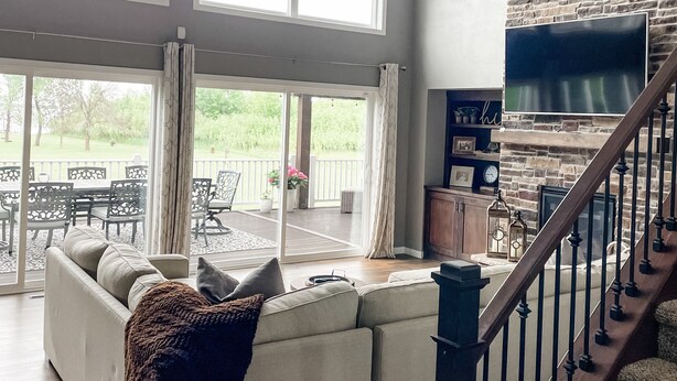 A spacious living room with a large sectional sofa, a ceiling fan, and a stone wall. - Luxurious Lakefront Escape – Premier EAA Rental with Breathtaking Views (Winneconne)