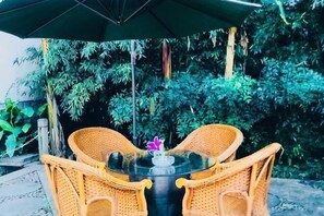 A wicker table with two chairs and a glass top, surrounded by lush greenery. - Longjing No.3 Resort (Hangzhou)