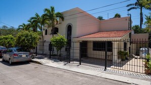 Una casa de dos pisos con techo de tejas, patio delantero cercado y un coche estacionado.