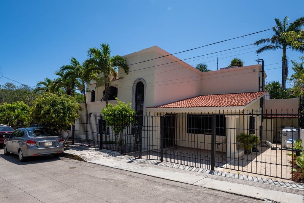 A two-story house with a tiled roof, a fenced front yard, and a parked car.
