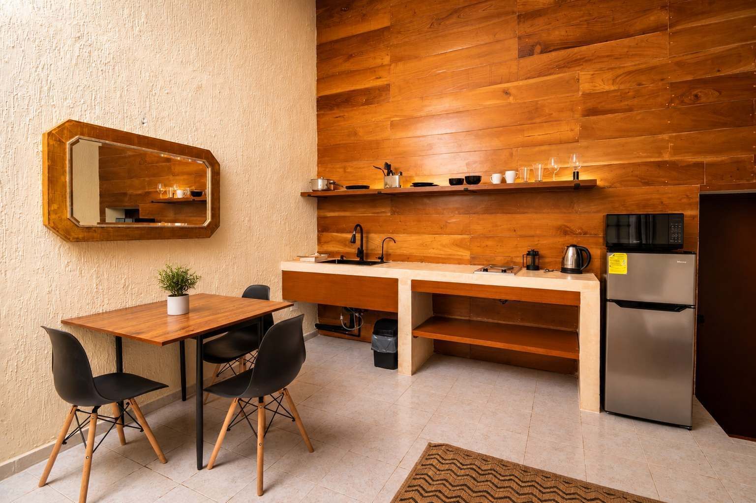 A compact kitchen with a wooden countertop, a sink, a refrigerator, and a dining area with chairs.