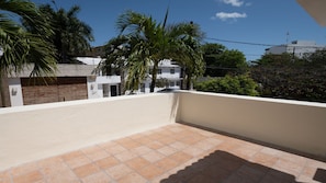 A balcony with tiled flooring, surrounded by buildings and palm trees.