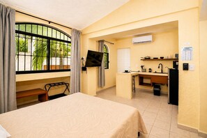 A hotel room with a bed, a desk, a television, and a kitchenette. - Cozy Cancún Studio with Outdoor Dining & Park View (Cancún)