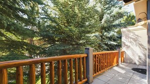A wooden balcony with a tiled floor, surrounded by dense evergreen trees. - Sun Valley 3BR - Hot Tub - 5min to River Run - Premium Snow Star Complex (Ketchum)