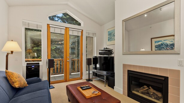 A living room with a sofa, a coffee table, a fireplace, a TV, and a balcony with glass doors. - Sun Valley 3BR - Hot Tub - 5min to River Run - Premium Snow Star Complex (Ketchum)