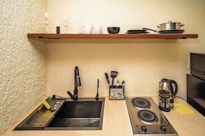 A kitchen with a sink, stove, and a shelf above the counter holding cups and a pot.