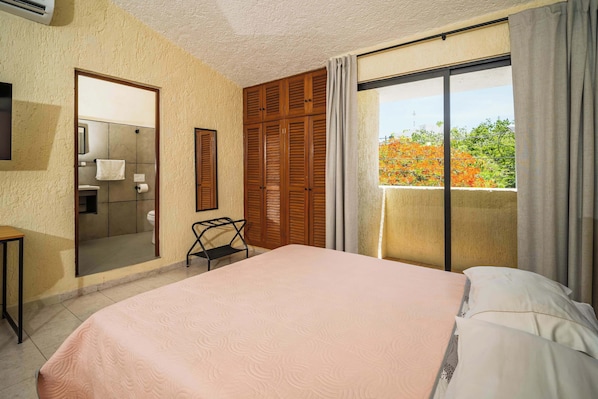 A bedroom with a bed, a small table, a mirror, a wardrobe, and a balcony with a view.