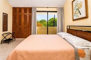 A bedroom with a bed, a chair, a balcony with curtains, and a framed picture on the wall.