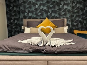 Een bed met een hoofdbord met een geometrisch patroon, een handdoek gedecoreerd in de vorm van een hart en een geel kussen.