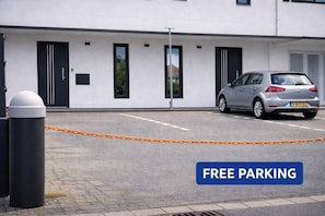 A modern building with a silver car parked in front, a 'FREE PARKING' sign, and a chain barrier.