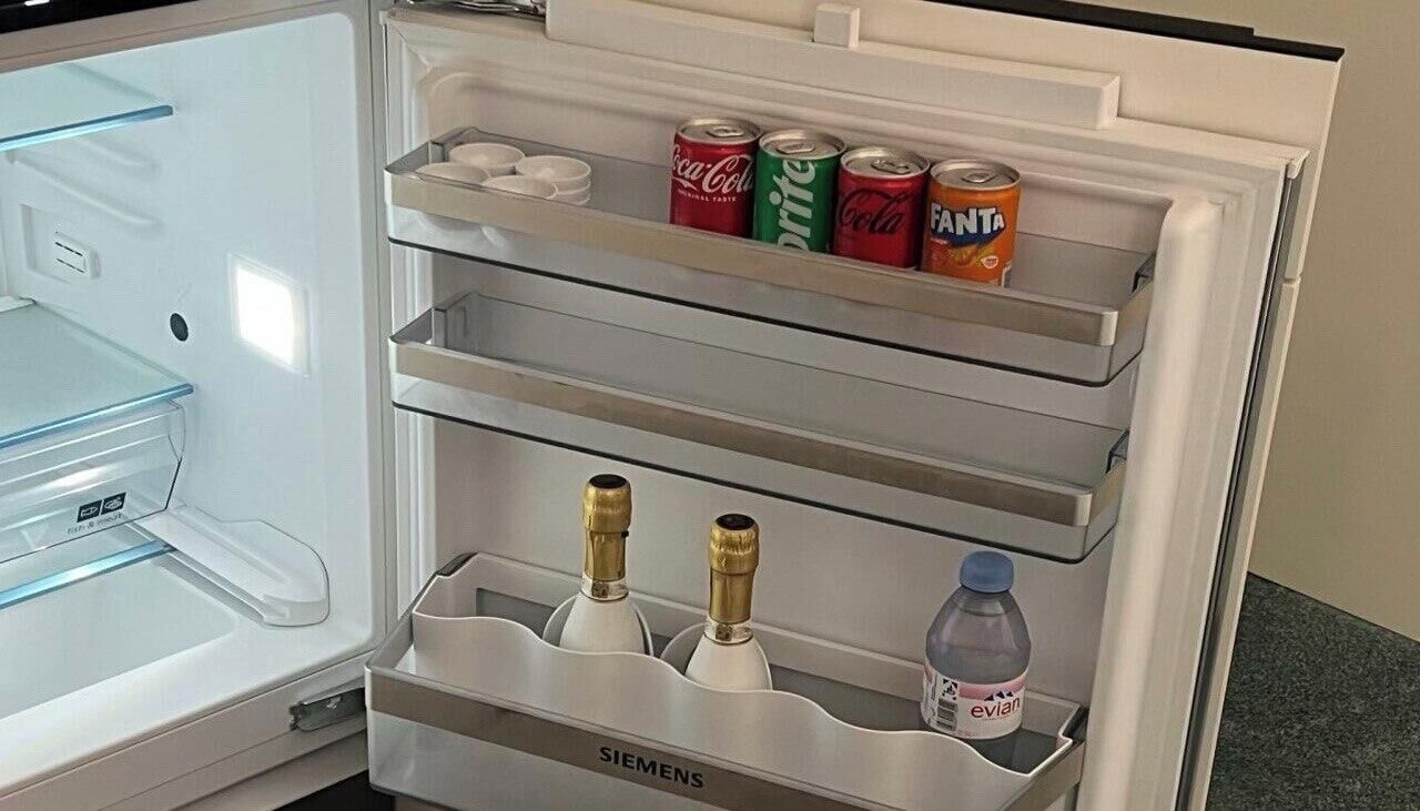 An open refrigerator with multiple shelves, containing beverages and bottles.