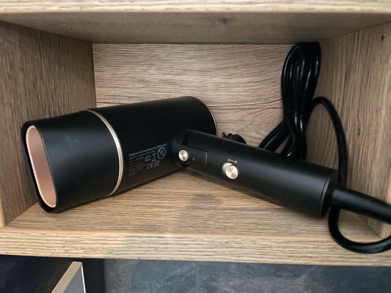 Un dispositivo cilíndrico negro con cable sobre una repisa de madera.