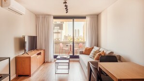 Una sala de estar moderna con sofá, una mesa de comedor, televisor y un balcón con sillas.