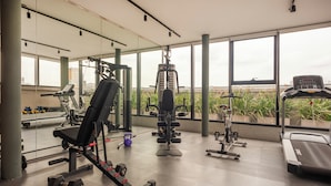Un gimnasio con diverso equipo de ejercicio, amplias ventanas y vistas a la ciudad.