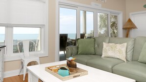 A living room with a green sofa, a white coffee table, and a view of the ocean through large windows. - Sailor's Dream (Port St. Joe)