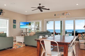 A spacious living area with a wooden dining table, white chairs, a green sofa, and a television. - Sailor's Dream (Port St. Joe)
