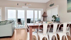 A dining area with a wooden table and white chairs, a ceiling fan, and a view of the ocean through large glass doors. - Sailor's Dream (Port St. Joe)