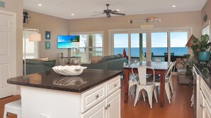 A kitchen with a central island, a dining area with a table and chairs, a television, and a view of the ocean. - Sailor's Dream (Port St. Joe)