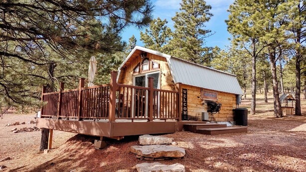 Un chalet rustique doté d’une terrasse en bois, d’un toit en métal et d’une pancarte indiquant « Bienvenue ».