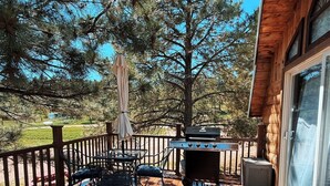 Une terrasse en bois, dotée de mobilier d’extérieur, d’un barbecue et offrant une vue sur les arbres.