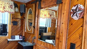 L’intérieur d’un chalet rustique, avec des murs en bois, une porte coulissante à miroir, un petit lavabo et une pancarte de bienvenue.