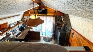 Une pièce mansardée chaleureuse avec un plafond en bois rustique, un luminaire suspendu et une cheminée en pierre.
