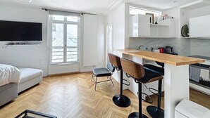 A modern kitchen with a wooden bar counter, a dining area with bar stools, a sofa, and a TV mounted on the wall. - Paris 8 Madeleine beauty (Paris)