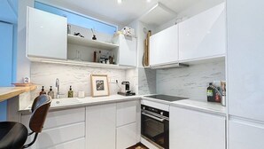 A modern kitchen with white cabinets, a built-in oven, a sink, and a wooden dining table with a chair. - Paris 8 Madeleine beauty (Paris)