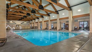 Una piscina interior con agua cristalina, vigas de madera y sillas de descanso.