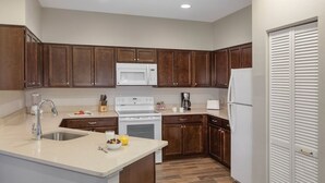 Una cocina con armarios de madera oscura, un microondas blanco, una estufa y un refrigerador.
