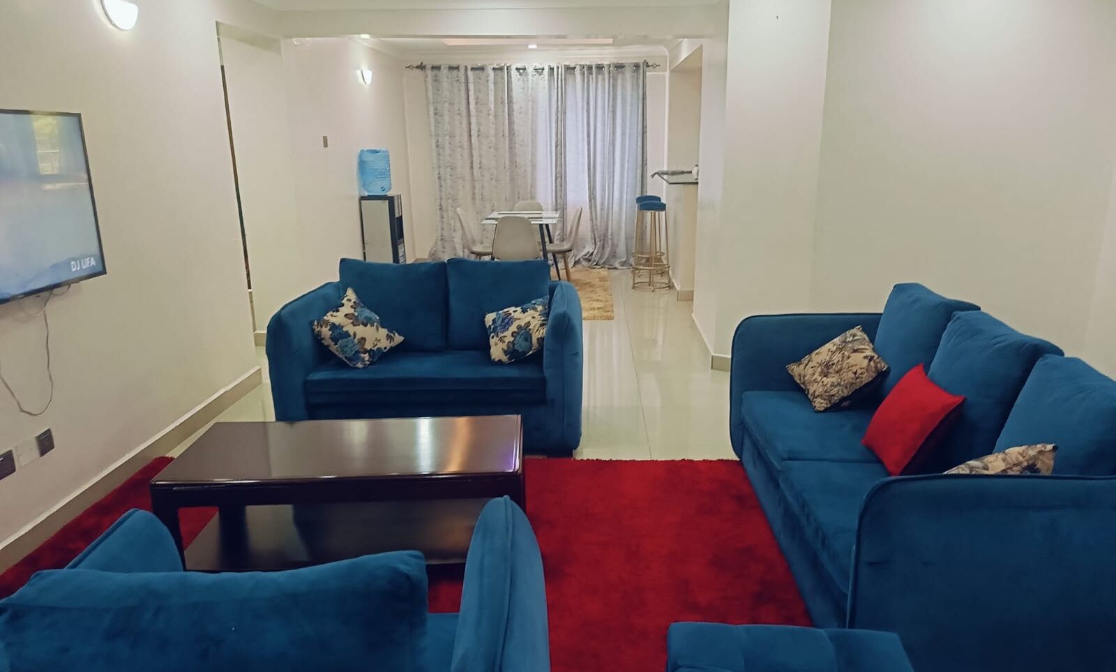 Ein modernes Wohnzimmer mit zwei blauen Sofas, einem roten Teppich und einem an der Wand befestigten Flachbildfernseher.