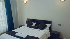 A neatly made bed with white bedding and brown pillows, a dark headboard, and a bedside table with a lamp.
