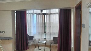 A room with two chairs, a small table, and a large window with sheer curtains.