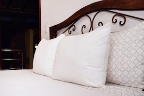 A bed with white bedding and two pillows, one plain and one with a pattern.