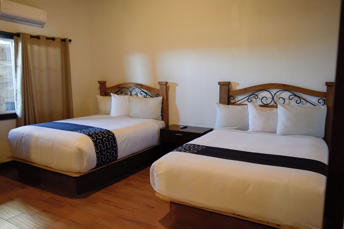 Dos camas individuales con cabeceros de madera y ropa de cama blanca, un suelo de madera y una ventana con cortinas.