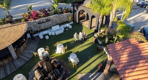 An outdoor seating area with round tables and chairs, a stone wall with the name 'SELAH', and a decorative fountain. - Finca Selah (Valle de Guadalupe)