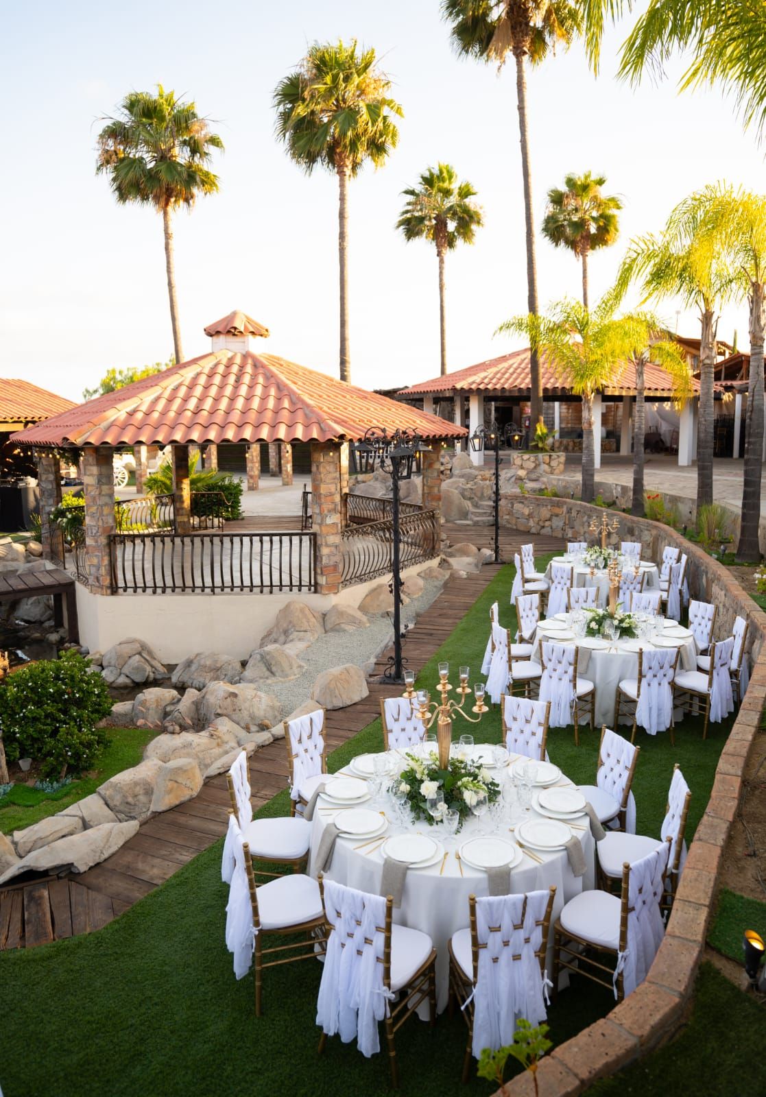 An outdoor wedding venue with round tables, white chairs, and a stone pathway.