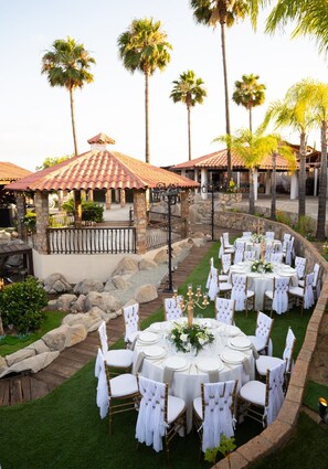 An outdoor wedding venue with round tables, white chairs, and a stone pathway. - Finca Selah (Valle de Guadalupe)